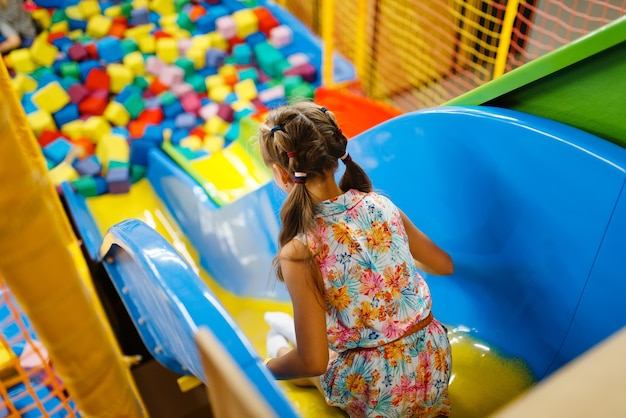 Niña montando en tobogán plástico para niños, parque infantil en el centro de entretenimiento