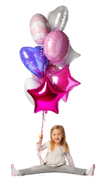 Niña con un montón de globos sentado aislado sobre superficie blanca