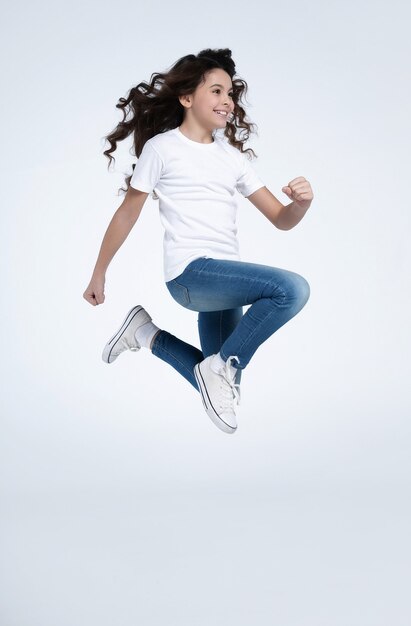 Foto la niña morena emocionada y feliz está saltando y gritando en camisetas blancas y jeans aislados sobre fondo blanco.