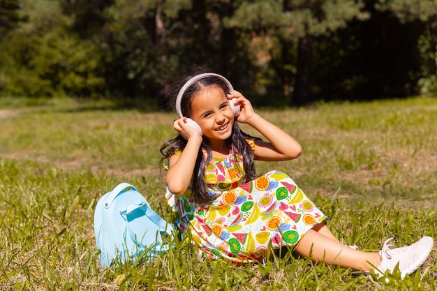 Niña morena escucha música en el parque sobre la hierba.