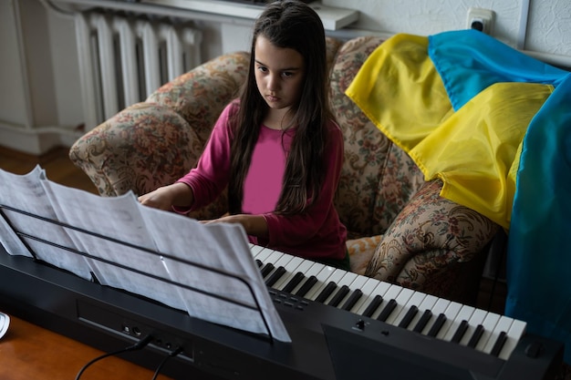 niña morena tocando el piano con notas con bandera de ucrania en casa.