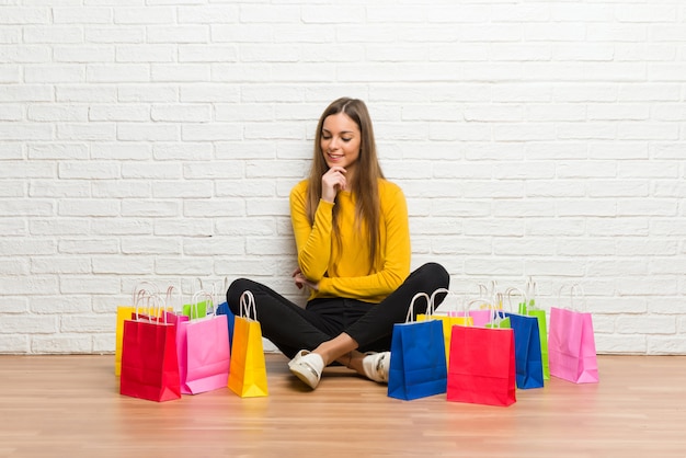 Niña con muchas bolsas de compras mirando hacia abajo con la mano en la barbilla