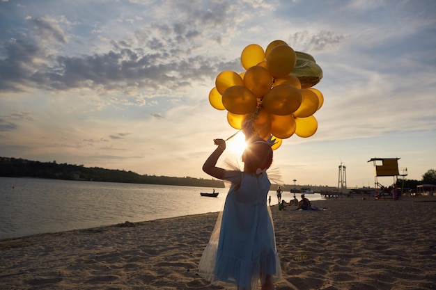 Niña con muchos globos dorados en la playa al atardecer