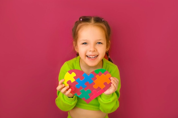 Niña muestra corazón de rompecabezas un símbolo de apoyo para niños con síndrome de autismo