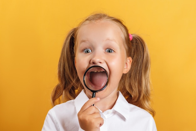 La niña muestra los dientes y sonríe con una lupa.