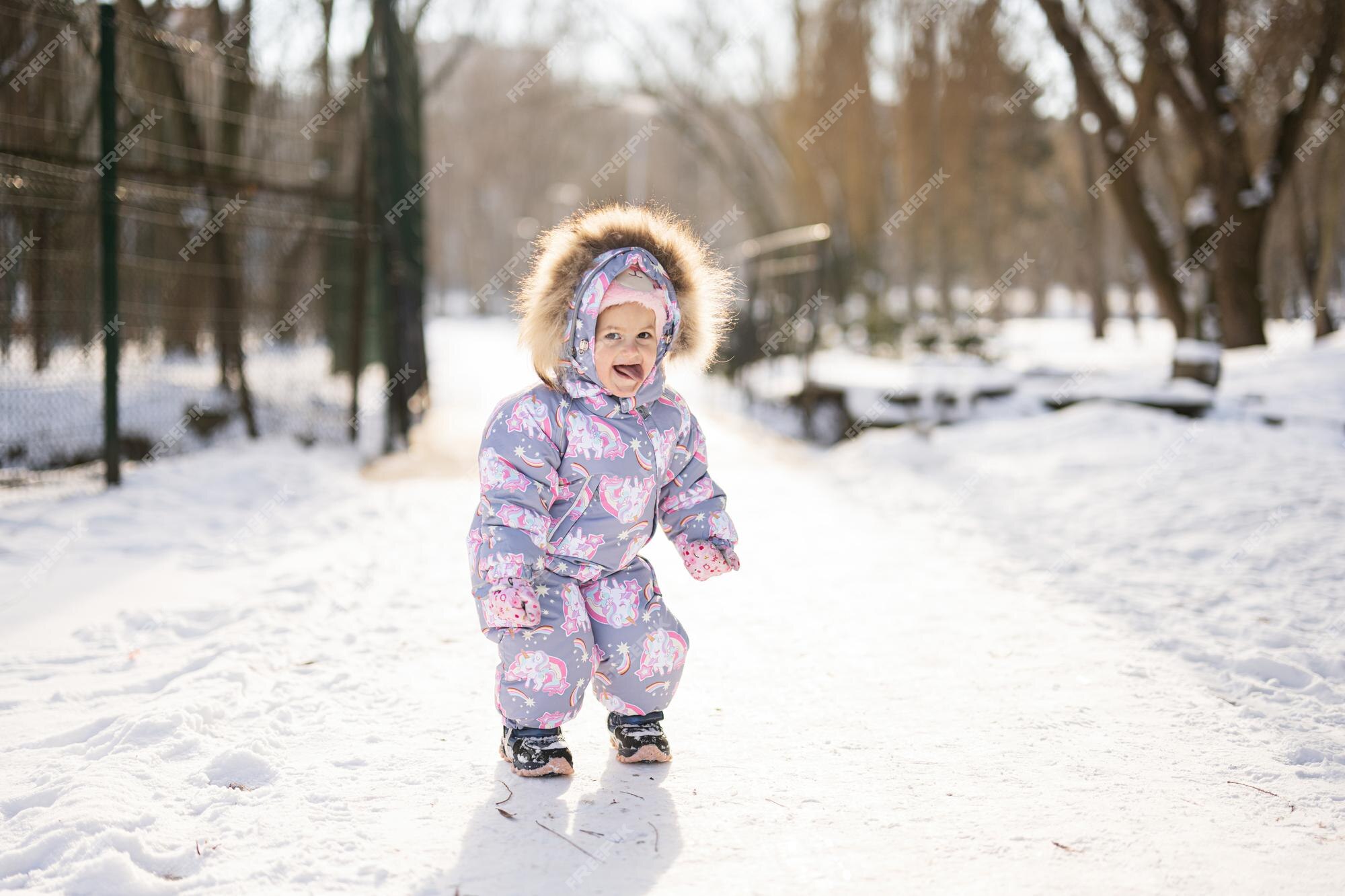 La niña muestra la lengua y usa un traje para niños en un día soleado de invierno helado | Foto Premium