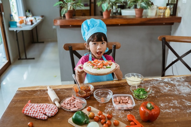 Niña muestra una pizza en la mesa de la cocina