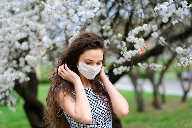 Niña, mujer joven en una máscara médica protectora estéril en su rostro en el jardín de primavera