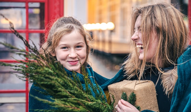 Una niña y una mujer joven con ramas de thuja y un regalo debajo de un plaid.