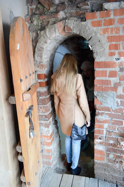 Foto una niña, una mujer, quedará atrapada en una gran puerta de madera gruesa y resistente con un arco en una pared de ladrillos de piedra