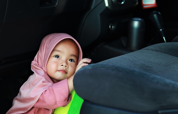 La niña musulmana está jugando debajo del asiento del auto.