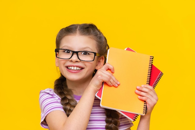 Una niña muy hermosa con coletas y anteojos muestra cuadernos y sonrisas