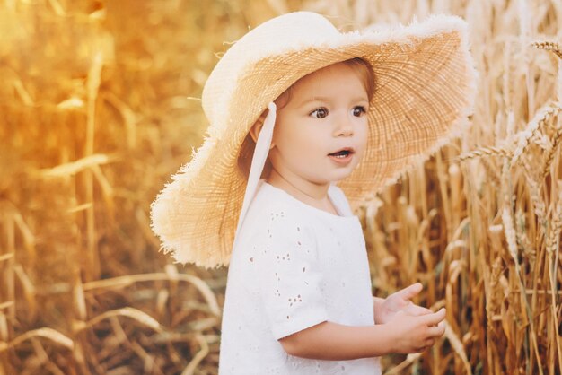 Niña muy linda con una hermosa sonrisa con sombrero de paja de verano en un paseo por los campos de trigo enfoque selectivo