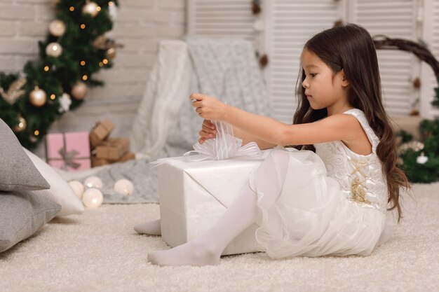 Niña muy sonriente abriendo caja grande con regalo de Navidad en casa