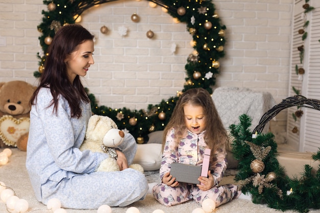 Niña muy sonriente con madre abriendo caja mágica con regalo de Navidad en casa