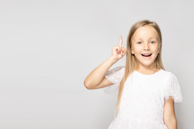 Niña muy sonriente de pie sobre fondo gris claro con el dedo levantado hacia arriba Banner con espacio de copia