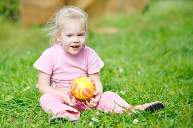 Una niña muy sonriente sentada en la hierba verde con la pelota