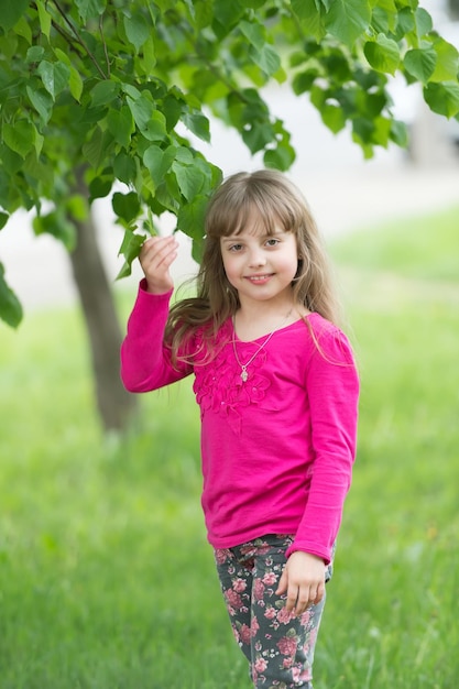 Niña en la naturaleza de pie bajo el árbol, sonriendo y mirando a la cámara