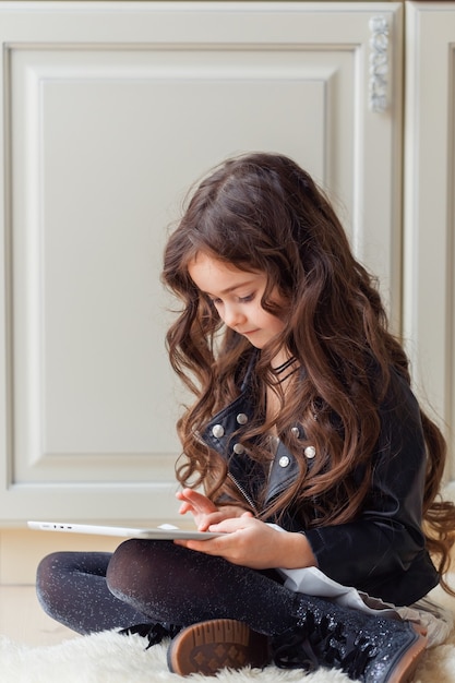 Una niña navega por Internet usando una tableta mientras está sentada en el piso de su habitación