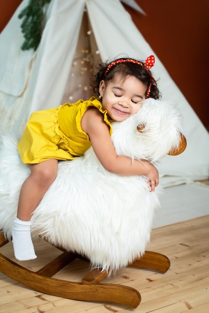 Niña negra africana se mece en un bebé de oveja caballito de madera con piel oscura sonriendo