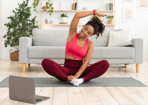 Niña negra de fitness haciendo ejercicio en la computadora portátil teniendo entrenamiento en línea en casa mantenerse en forma concepto
