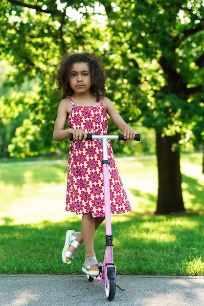 Niña negra con un patinete en un parque de la ciudad