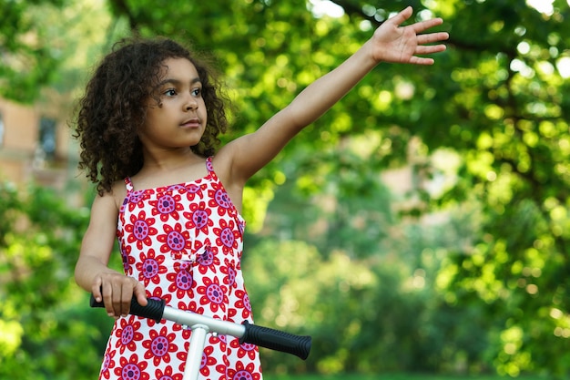 Niña negra con un patinete en un parque de la ciudad