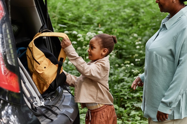 Niña negra poniendo mochila en el maletero del coche