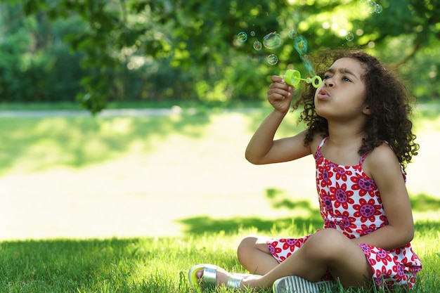 Niña negra soplando pompas de jabón en un parque de la ciudad