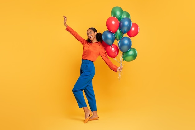 Foto niña negra sosteniendo un montón de globos de colores levantando el brazo estudio