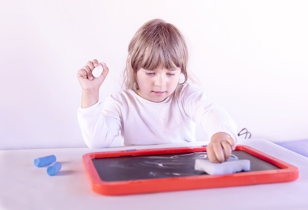 Niña niña borra el dibujo en la pizarra en casa