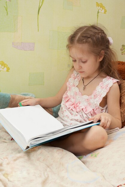 Niña niña sentada en una cama y mirando la página vacía del libro