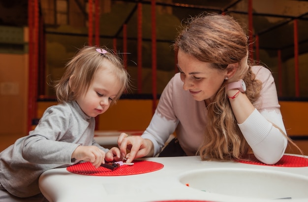 Niña con una niñera juega ladrillos de juguete en la mesa en un centro de entretenimiento para niños