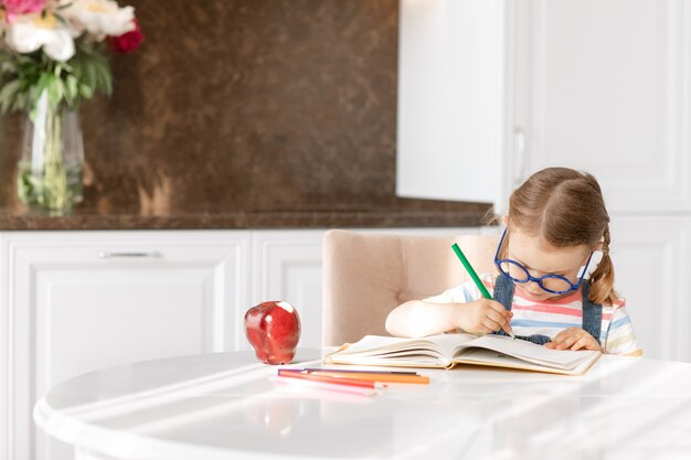 Niña niño aprender a escribirhacer los deberes sentarse a la mesa solo hacer notas dibujar lápices de colores