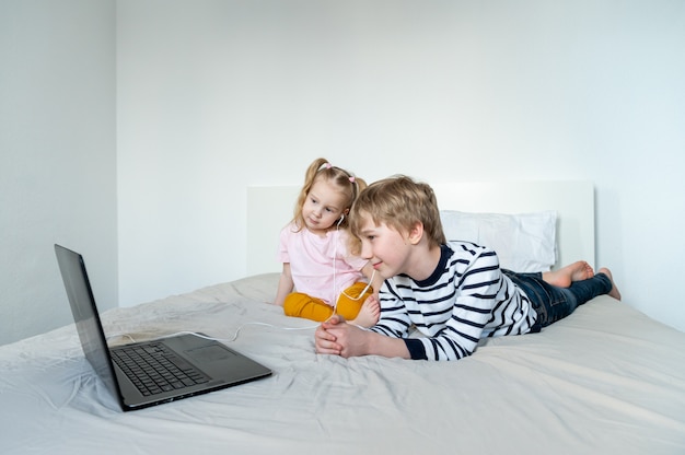 Niña y niño con auriculares amd portátil en casa