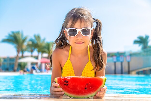 Niña niño come sandía cerca de la piscina