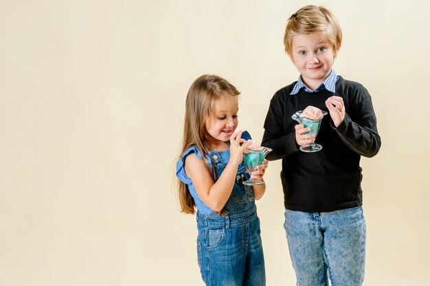 Niña y niño comen helado sobre un fondo claro