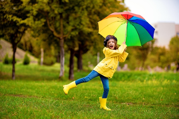 Niña niño divertido feliz con paraguas multicolor en botas de goma en el parque de otoño.