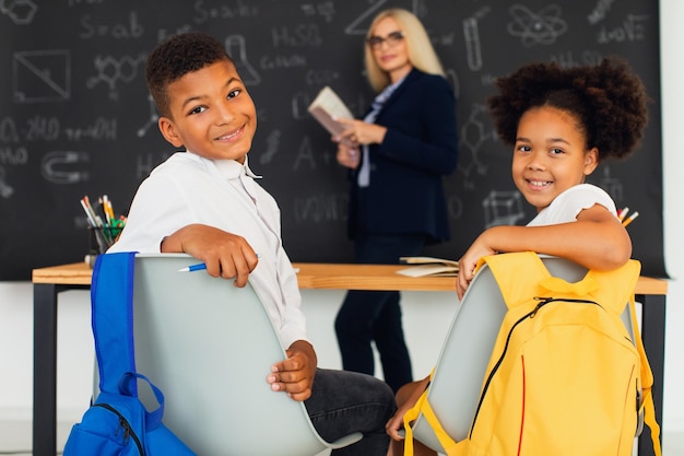 Una niña y un niño escolares afroamericanos resuelven problemas con el maestro durante una lección de regreso a la escuela