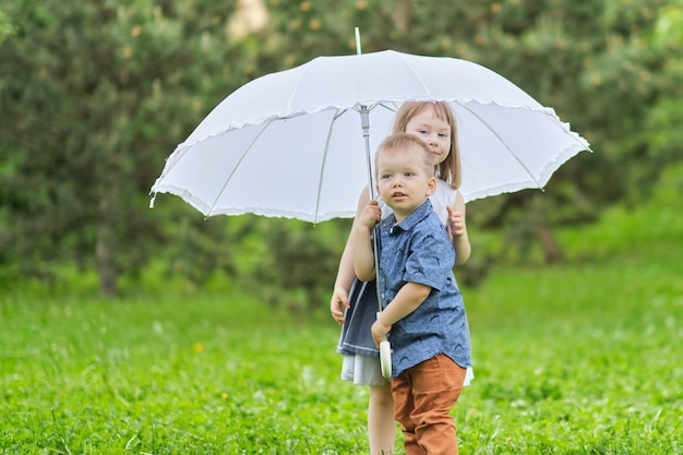 Niña y niño se esconden bajo un paraguas hermano y hermana juegan en el parque