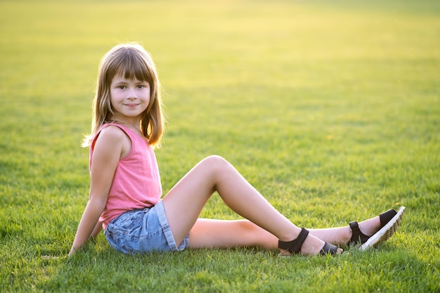 Niña niño feliz descansando mientras está sentado en el césped de hierba verde en un cálido día de verano.