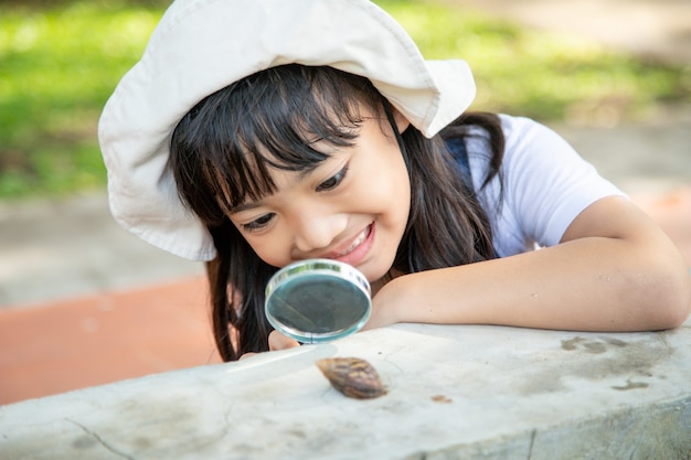 Niña niño feliz explorando la naturaleza con una lupa y un caracol. Se divierte en el jardín. El concepto de niño está listo para ir a la escuela.