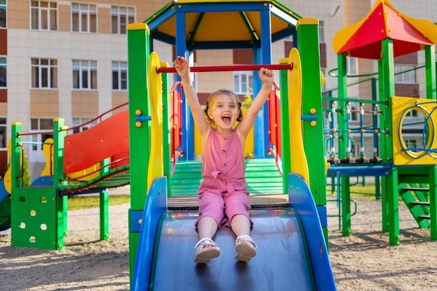 Una niña niño feliz juega en el parque infantil del complejo cerca de la casa en el verano en el patio y sonríe