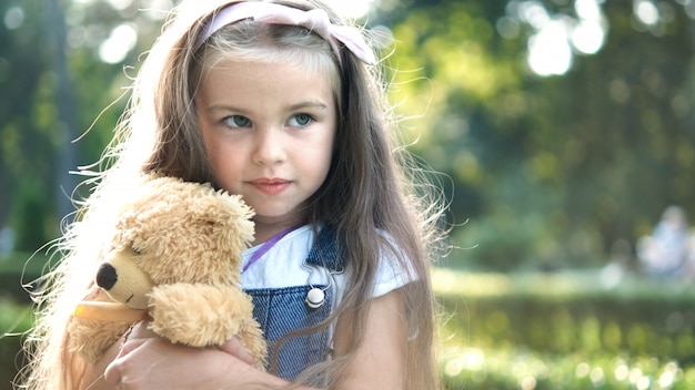 Niña niño feliz jugando con su osito de peluche favorito al aire libre en el parque de verano.