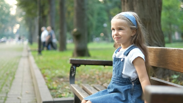 Niña niño feliz sentado en un banco descansando en el parque de verano.