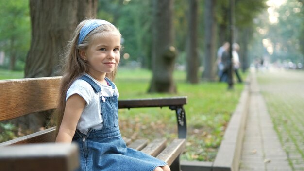 Niña niño feliz sentado en un banco descansando en el parque de verano.