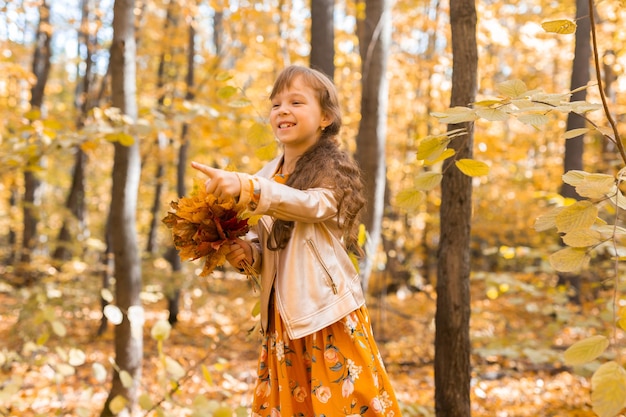 Niña niño con hojas de naranja otoñal en un concepto de temporada de otoño y niños de estilo de vida de parque