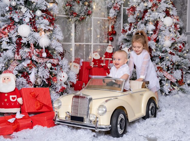 Niña y niño jugando con coche de juguete en la habitación decorada de Navidad.