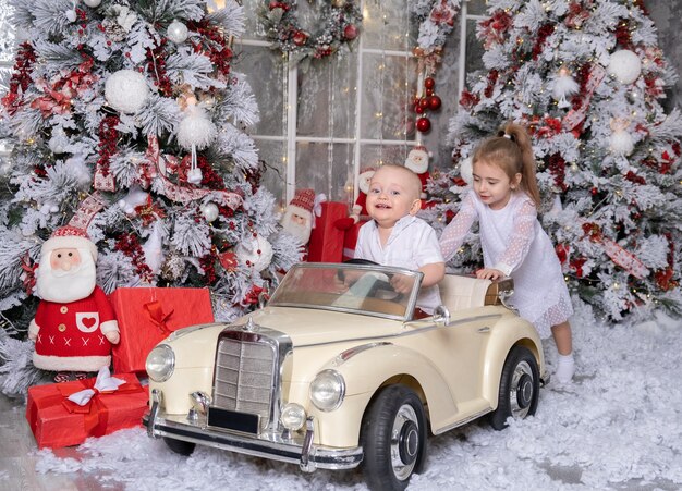 Niña y niño jugando con coche de juguete en la habitación decorada de Navidad.