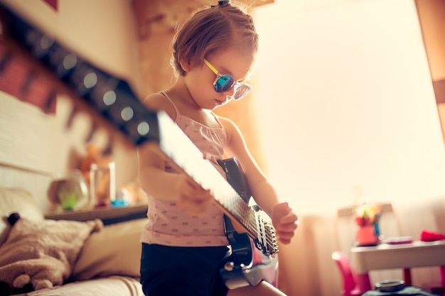 Niña niño lindo en gafas de sol tocando la guitarra.